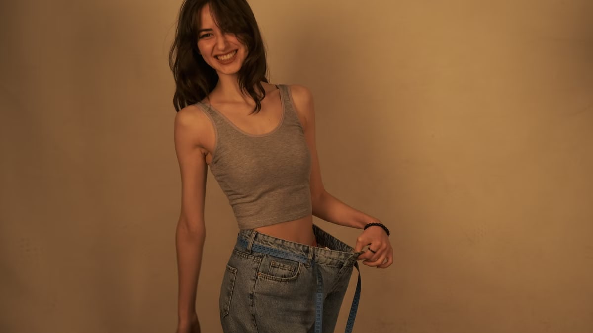 Joyful woman shows success in weight loss by wearing loose jeans. Healthy lifestyle concept.